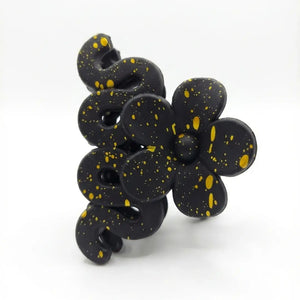 Side view of black artistic hair catcher with gold paint splatter and floral design.