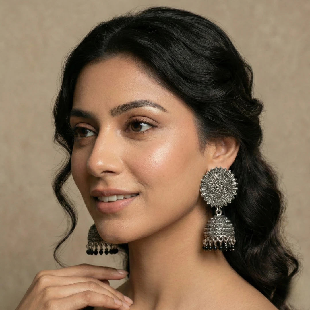 A model wearing antique silver Pakistani jhumkas with a floral sunburst stud and black beads, showcasing the elegant drop and traditional style from Applique Threads.