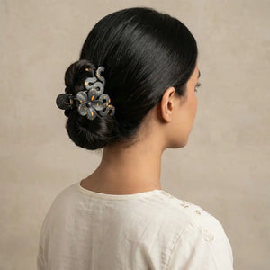 Woman wearing a matte black and gold speckled flower hair claw clip in a neat bun hairstyle.
