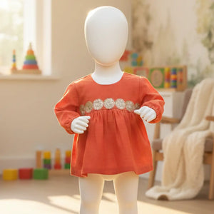 Toddler girl standing wearing rust orange cotton top with sequin chest detail and long sleeves.