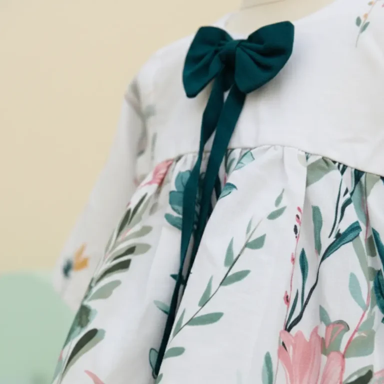 Close up detail of dark teal bow and botanical print on white girls dress