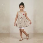 Aaliya in a playful pose wearing a beige and red floral sleeveless frock for girls, featuring a waist bow and rose detail.