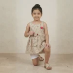 Candid kneeling pose of Aaliya showcasing the fabric texture and red floral print of the KIDS summer frock collection.
